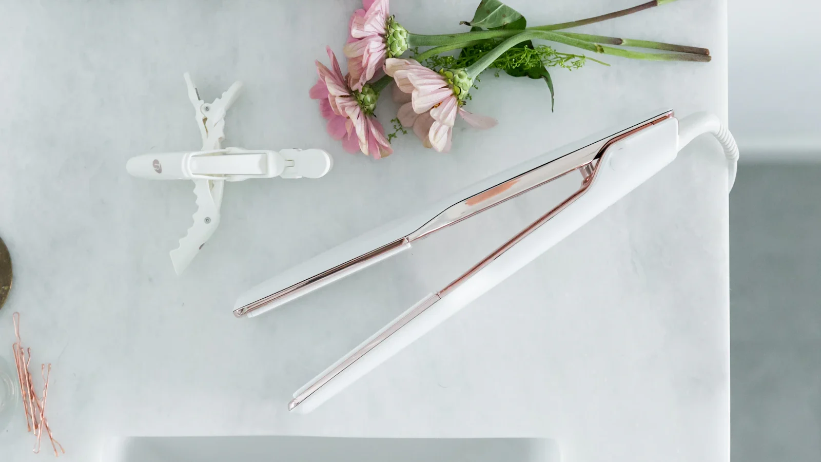 Lisseur et pinces à cheveux posés sur un plan de salle de bains à côté de fleurs roses